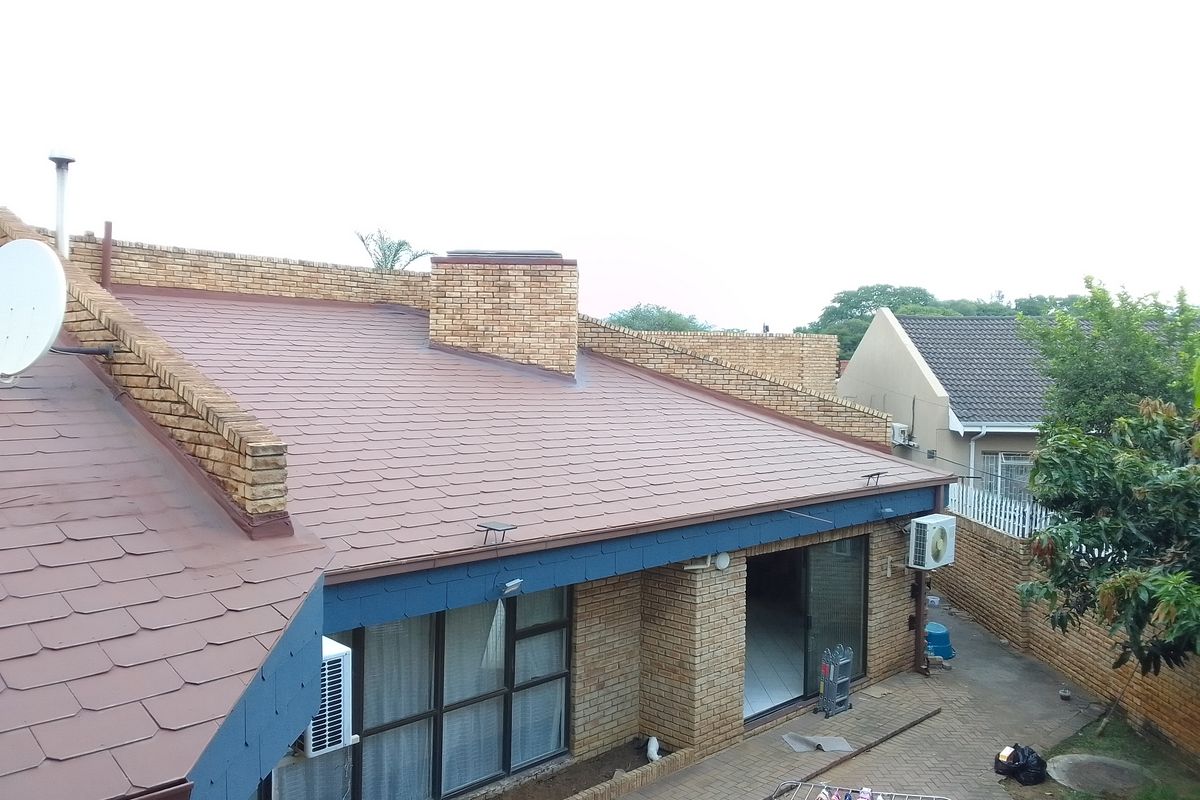 An elevated view of the rear exterior featuring a brick facade, tiled roof, and a paved patio area with sliding door access.