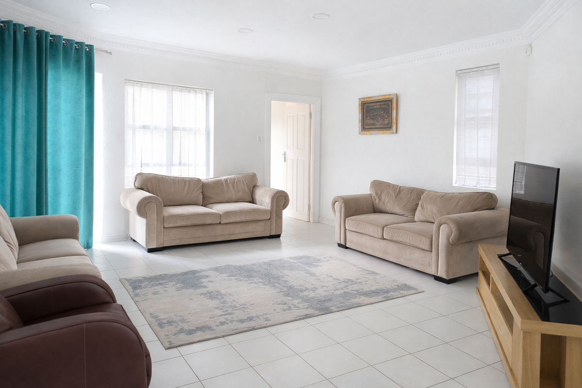 A bright and spacious living room featuring neutral tiled flooring, recessed downlighting, and decorative crown molding.