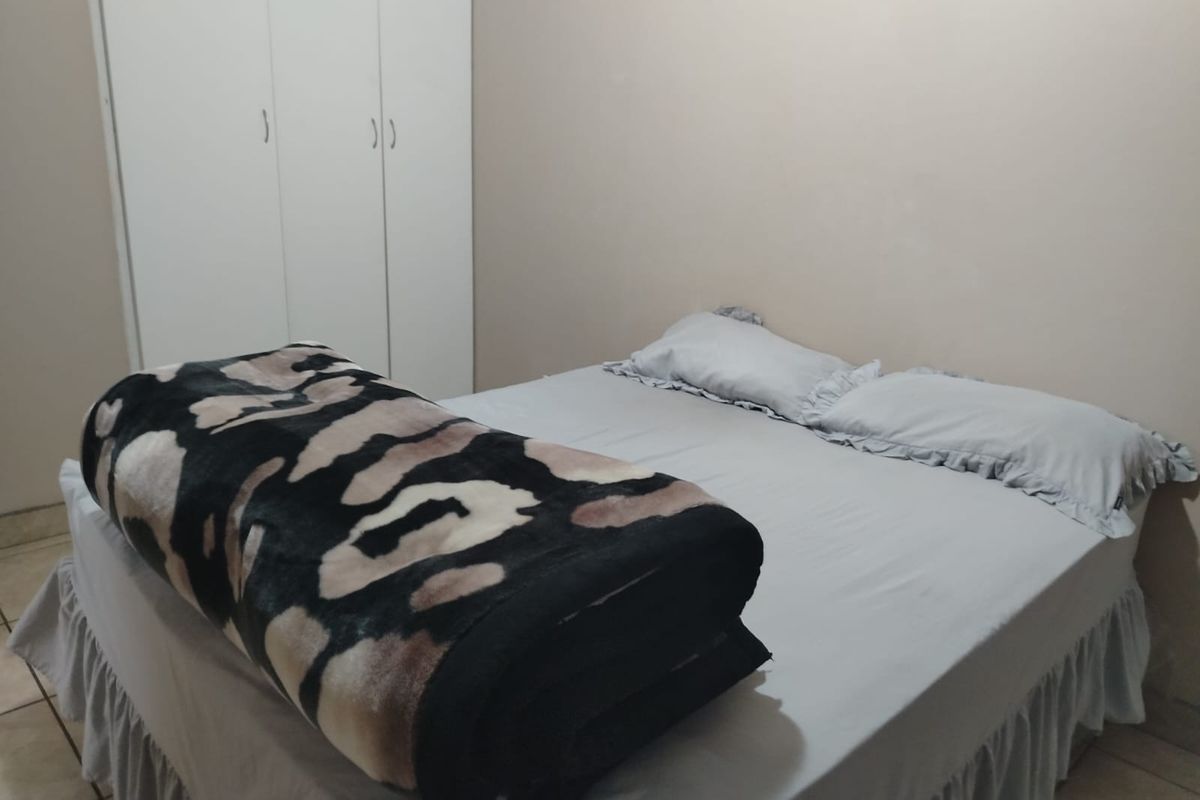 A functional bedroom featuring neutral wall finishes, tiled flooring, and a built-in wardrobe for storage.