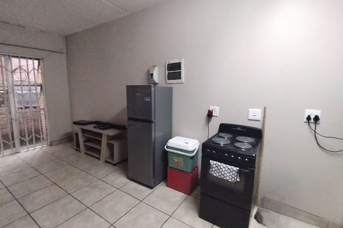 A basic kitchen area featuring tiled flooring, a freestanding electric stove, and a security gate, currently lacking built-in cabinetry and finished surfaces.