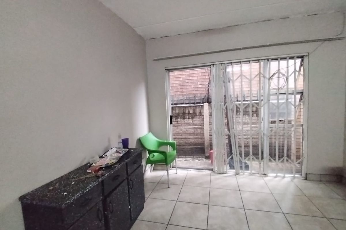 A sparsely furnished living area featuring tiled flooring, built-in cabinetry, and a sliding glass door with a security gate leading to an outdoor space.