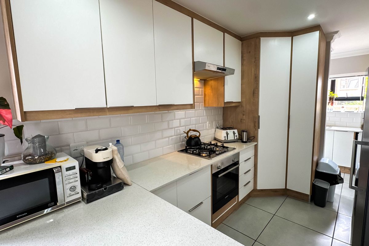 Modern kitchen featuring white cabinetry with wood-grain accents, subway tile backsplash, stone countertops, built-in oven, and gas hob with extractor fan.