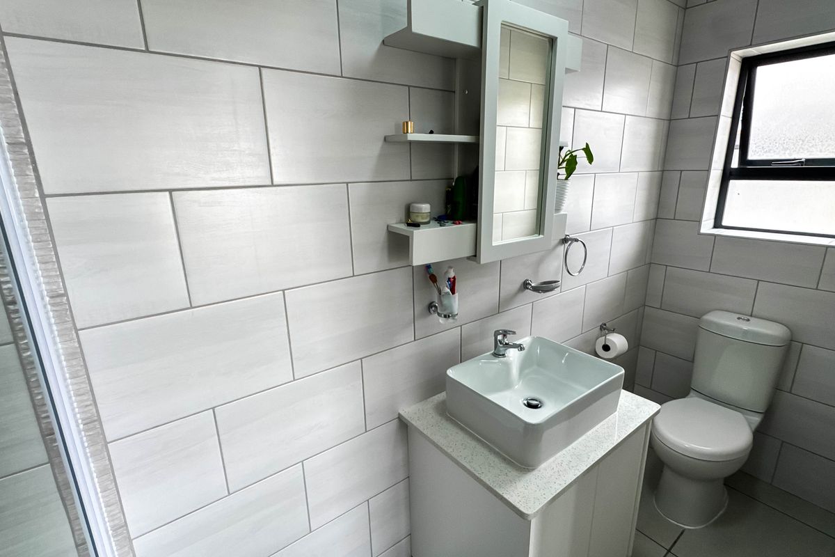 Modern bathroom featuring a vessel sink vanity, wall-mounted storage cabinet, and floor-to-ceiling light-toned tiling.