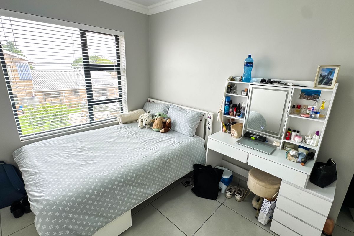 A well-lit bedroom featuring neutral wall tones, large window with fitted blinds, and tiled flooring.