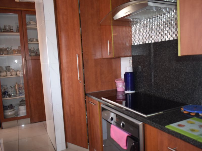 A functional kitchen featuring warm-toned wooden cabinetry, granite countertops, a built-in oven with hob, and a separate glass-fronted display cabinet.