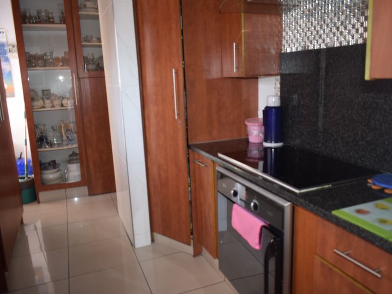 A functional kitchen featuring wood-finish cabinetry, granite countertops, a built-in oven, and a glass-fronted display cabinet with tiled flooring throughout.