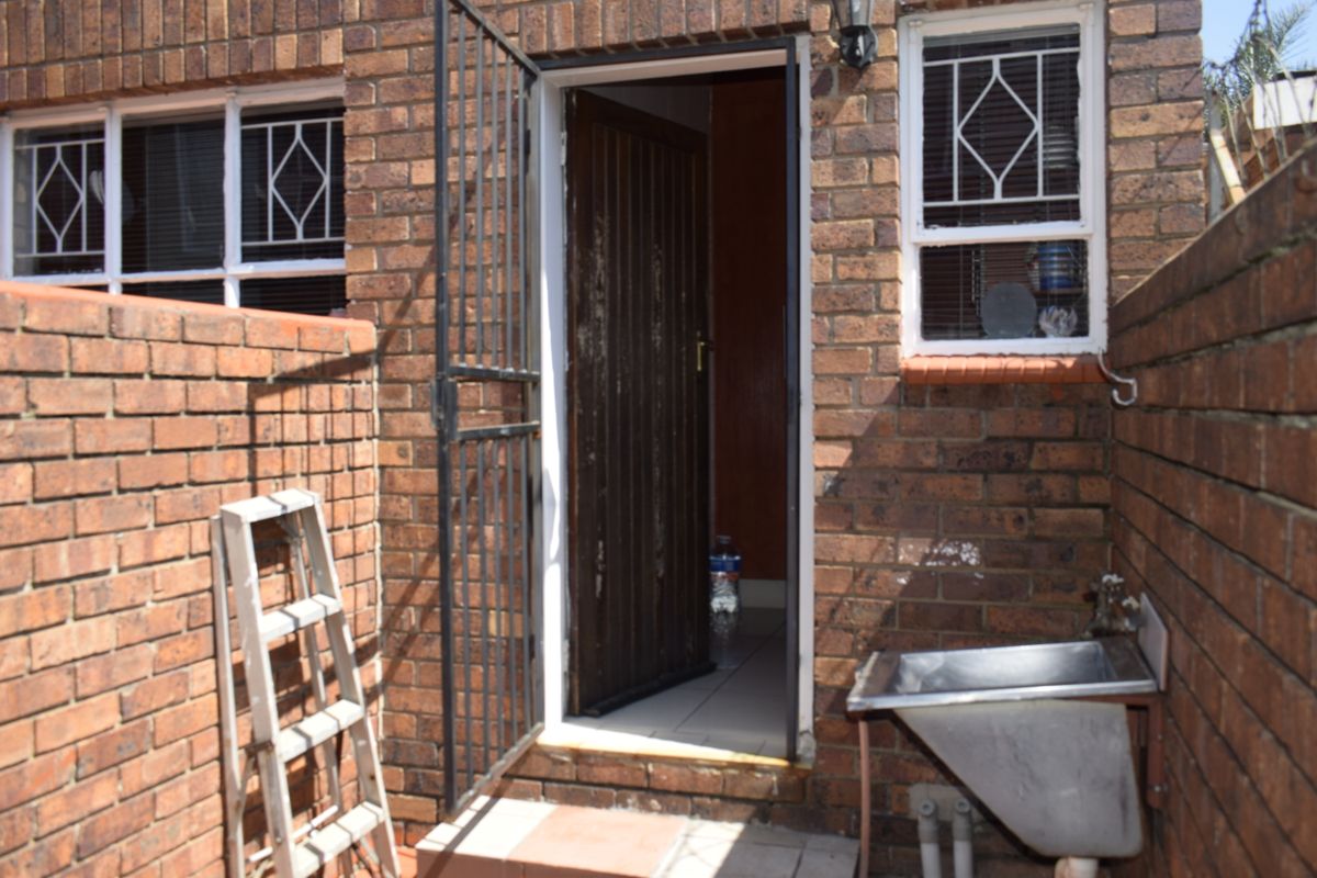 Rear exterior view of a townhouse featuring a brick facade, security gate, and a functional utility sink area.