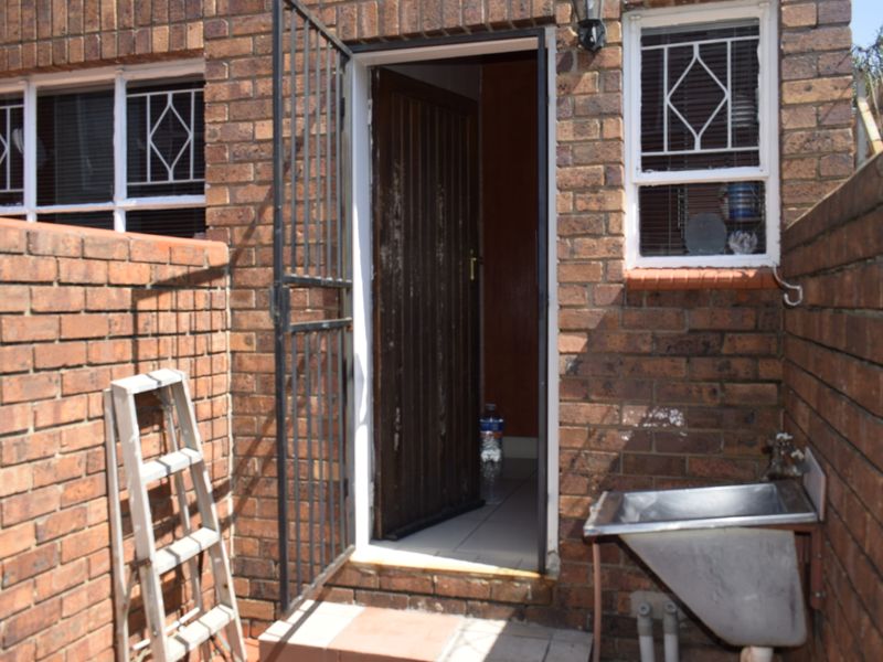 Rear exterior view of a townhouse featuring a brick facade, security gate, and a functional utility sink area.