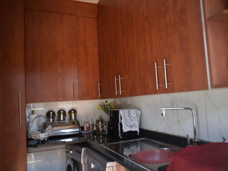 A functional scullery area featuring wood-look laminate cabinetry, granite countertops, a stainless steel sink, and a tiled backsplash.