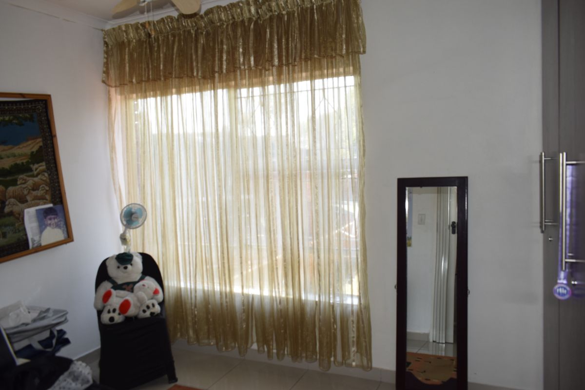 A bedroom featuring tiled flooring, a built-in wardrobe, and a large window fitted with security bars.