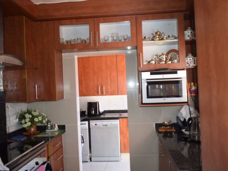 A functional kitchen featuring wood-finish cabinetry, granite countertops, and integrated appliances, with a separate scullery area visible through the doorway.