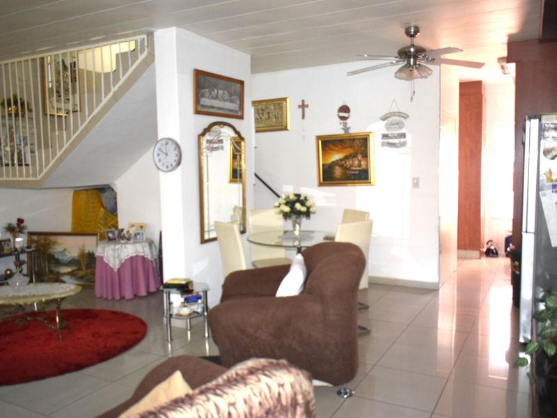 Open plan living and dining area featuring tiled flooring, a central staircase, and a ceiling fan.