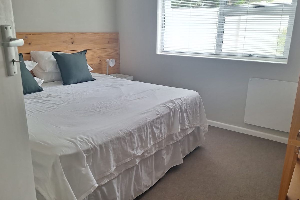 A functional bedroom featuring a built-in wooden headboard, neutral carpeting, and a wall-mounted heater beneath the window.