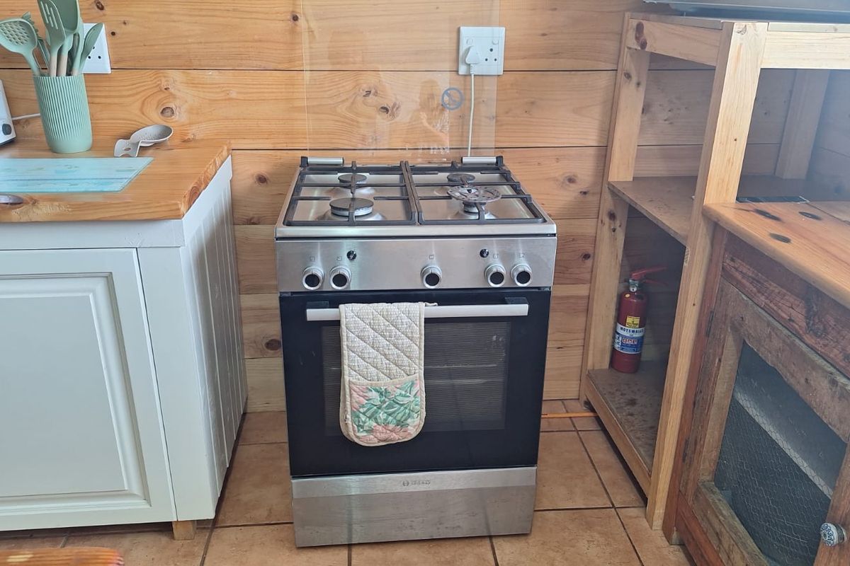 A kitchen area featuring timber wall cladding, tiled flooring, and a stainless steel freestanding gas stove with oven.