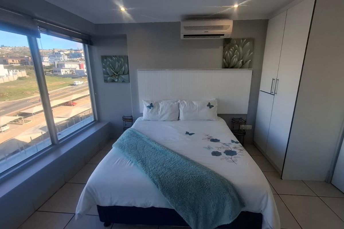 A well-lit bedroom featuring large floor-to-ceiling windows with expansive views, built-in cabinetry, and a wall-mounted air conditioning unit.