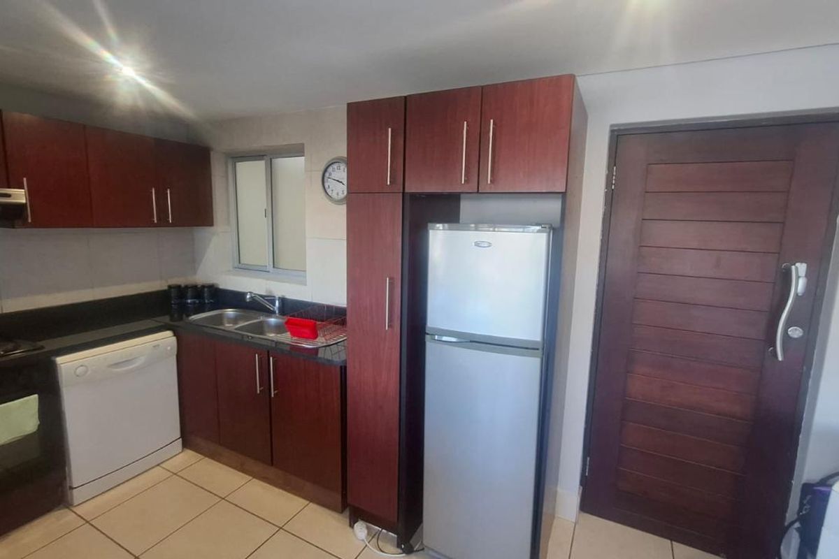 Compact kitchen featuring dark wood cabinetry, granite countertops, double sink, built-in oven, extractor fan, and tiled flooring with direct access to an exterior door.