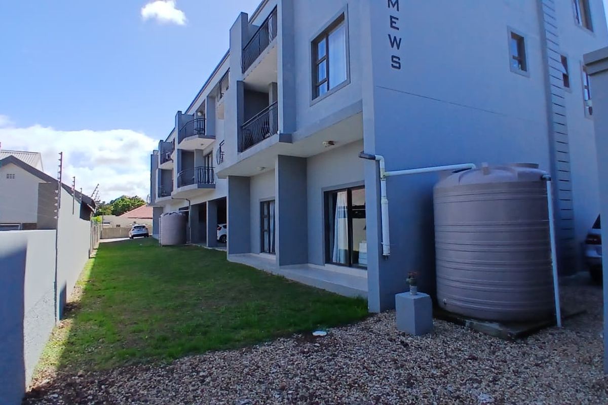 Rear view of a multi-story apartment complex featuring private balconies, sliding glass doors, and a communal garden area with water storage tanks.