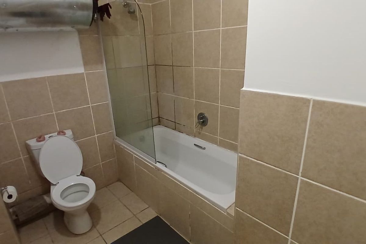 A functional bathroom featuring a bathtub with a glass screen, toilet, and neutral ceramic tiling throughout.