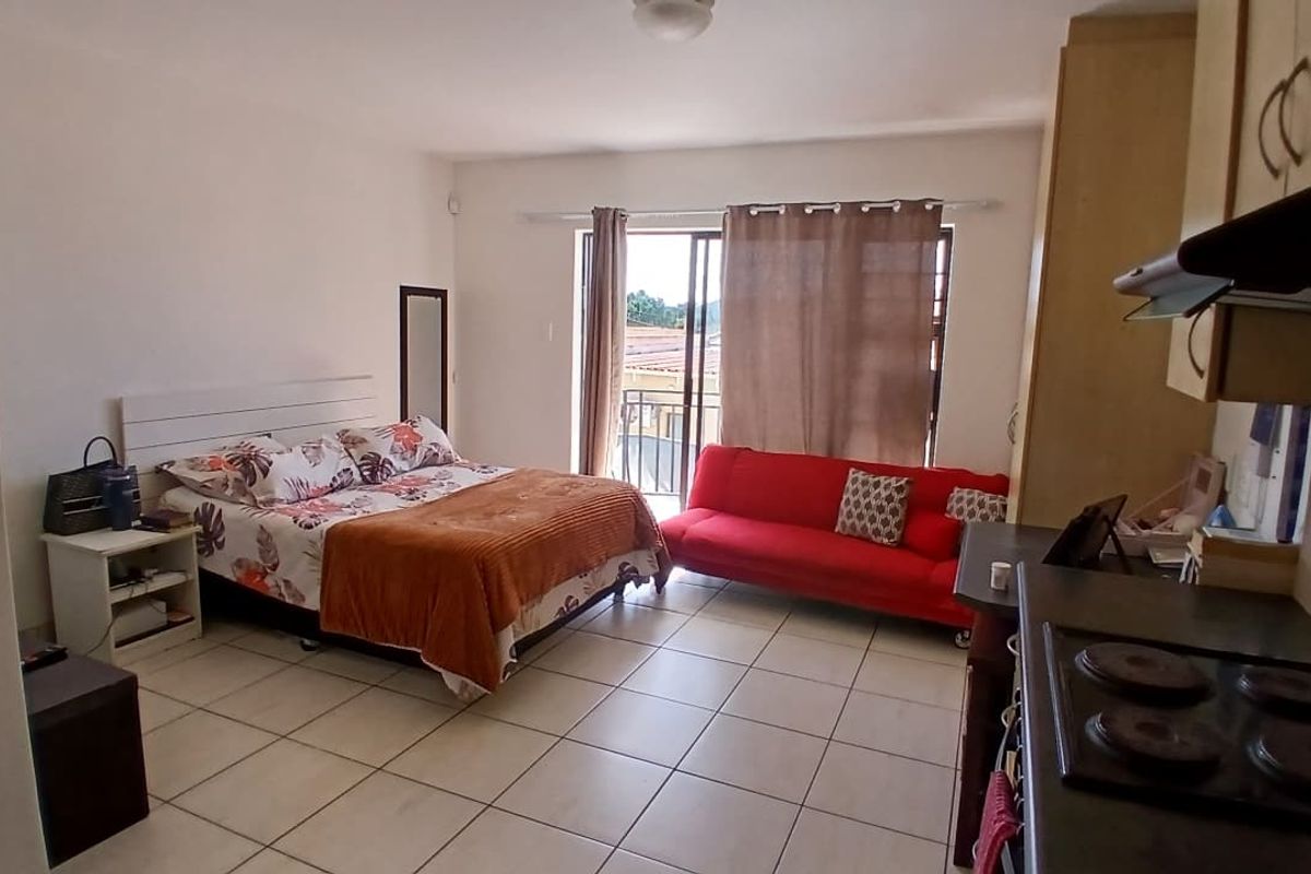 Open-plan studio apartment featuring tiled flooring, a functional kitchenette with built-in cabinetry, and direct access to a private balcony through sliding glass doors.