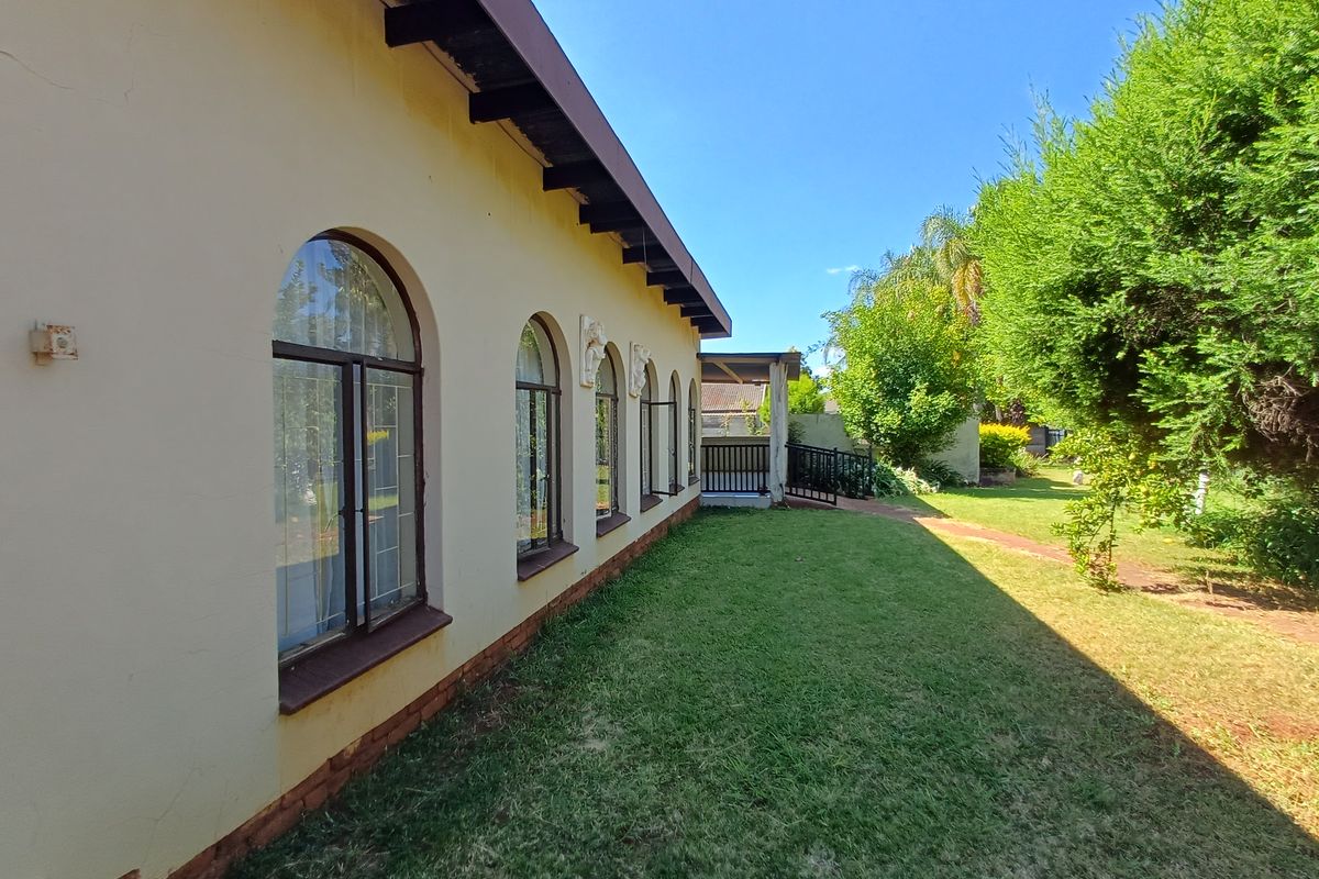 Rear view of the property featuring arched windows, exposed rafters, and a well-maintained garden area with a covered patio.
