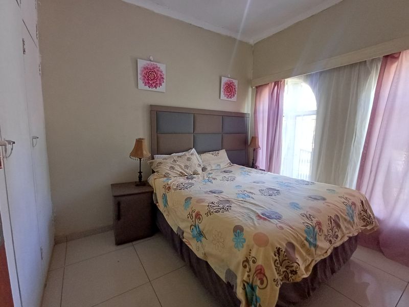 A bedroom featuring tiled flooring, built-in cupboards, and an arched window with curtains.