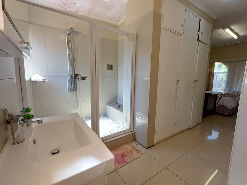Bathroom featuring a walk-in shower, vanity basin, and extensive built-in cupboard storage with tiled flooring throughout.