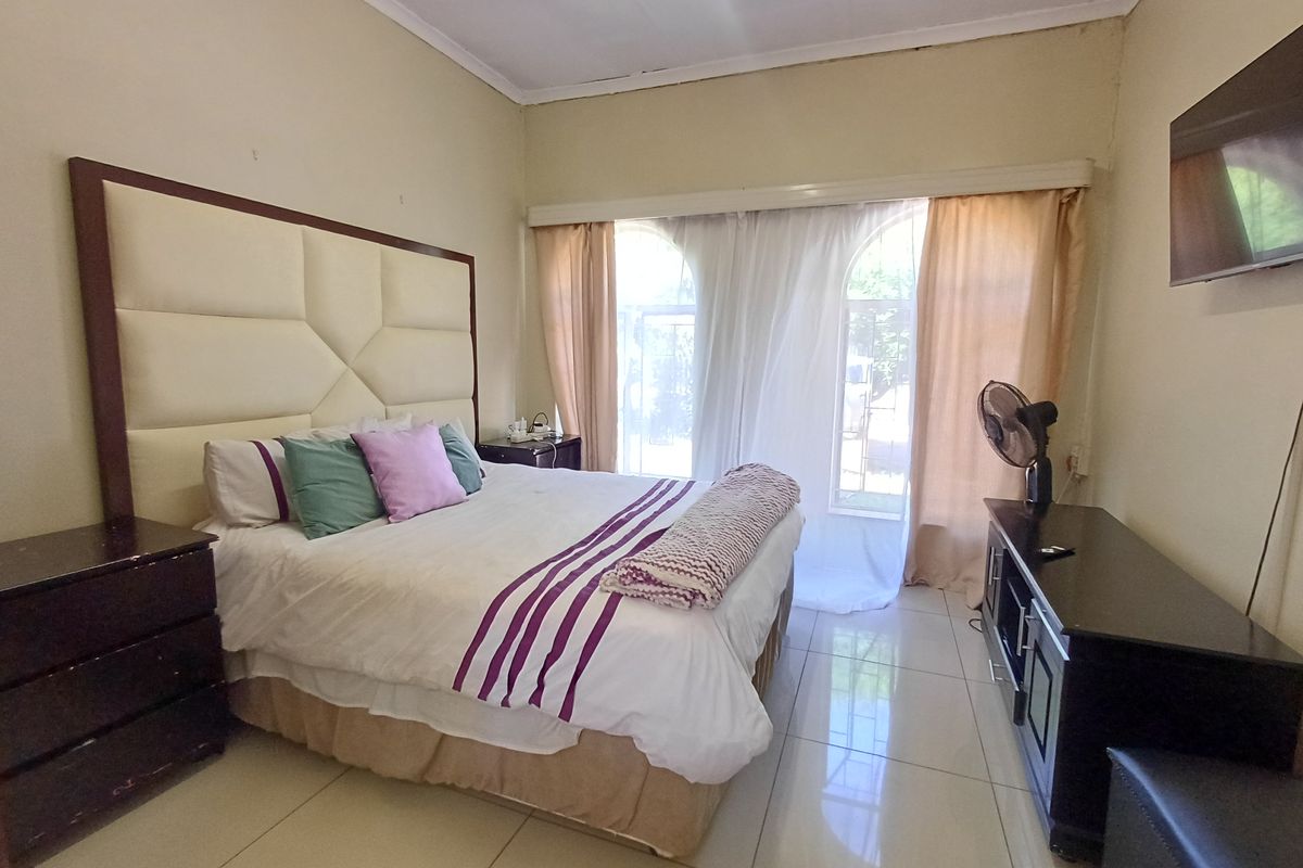 A bedroom featuring tiled flooring, arched windows with curtains, and a large upholstered headboard.