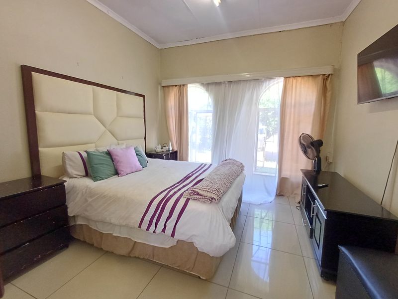 A bedroom featuring tiled flooring, arched windows with curtains, and a large upholstered headboard.