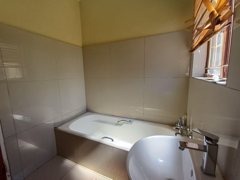 A functional bathroom featuring a built-in bathtub, a modern basin with a mixer tap, and neutral wall tiling.