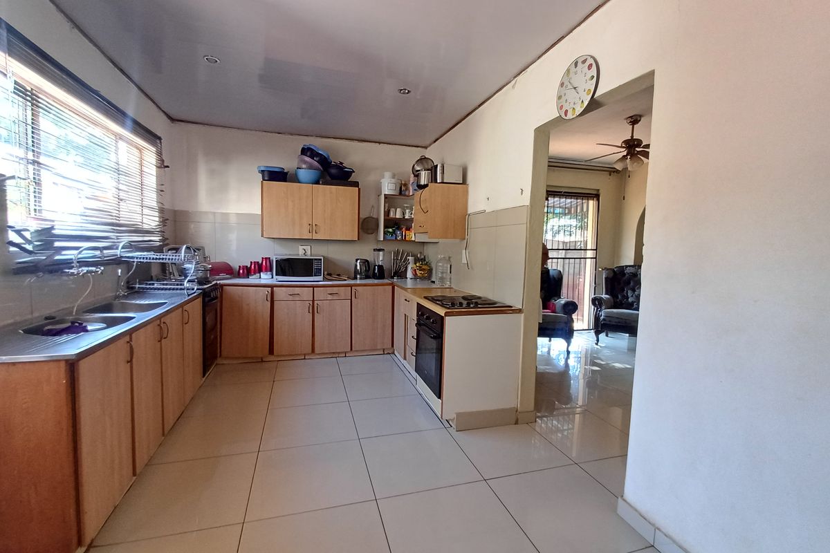 Functional kitchen featuring laminate cabinetry, built-in oven and hob, double stainless steel sink, and tiled flooring with a direct view into the adjacent living area.