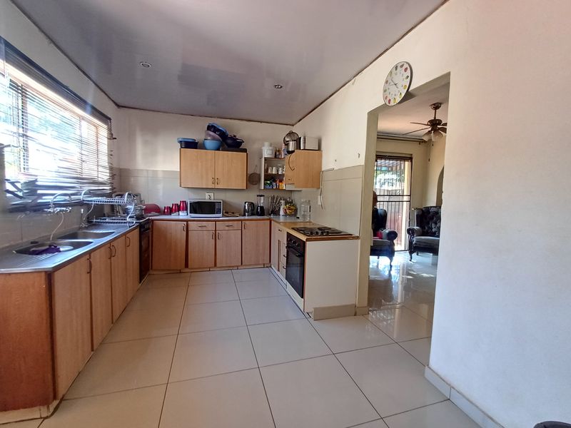 Functional kitchen featuring laminate cabinetry, built-in oven and hob, double stainless steel sink, and tiled flooring with a direct view into the adjacent living area.