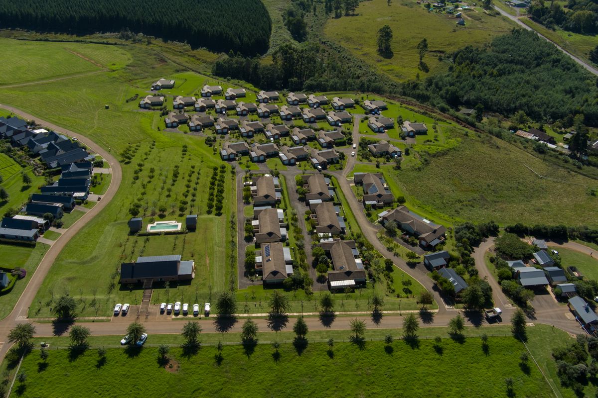 Aerial view of a residential townhouse complex featuring multiple units, paved access roads, landscaped green spaces, and a communal swimming pool.