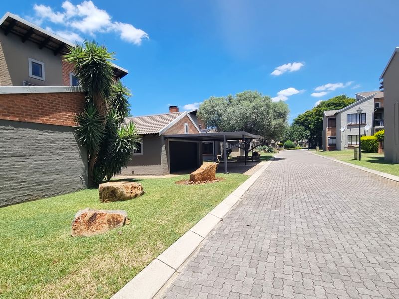 A view of the residential street within the complex, featuring paved driveways, carports, and well-maintained landscaped garden areas.