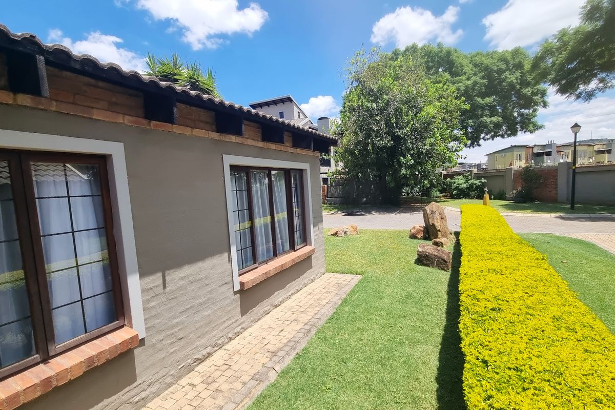A view of the rear exterior featuring a brick and plaster facade, tiled roof, paved walkway, and a well-maintained garden hedge.
