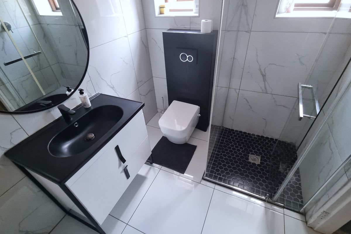 Modern bathroom featuring a wall-mounted toilet with concealed cistern, glass shower enclosure, and a contemporary vanity unit with a black basin.