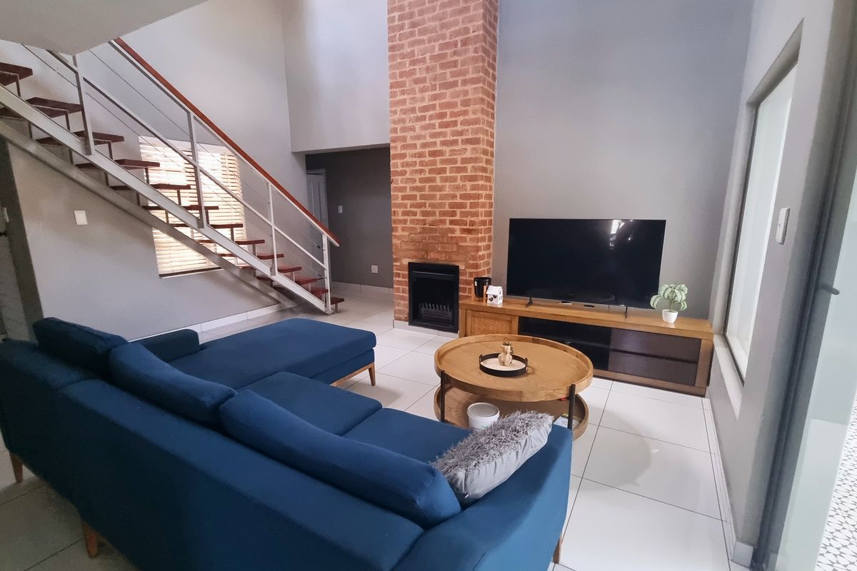 Spacious living room featuring a double-volume ceiling, an exposed brick fireplace, and a modern staircase with metal railings.