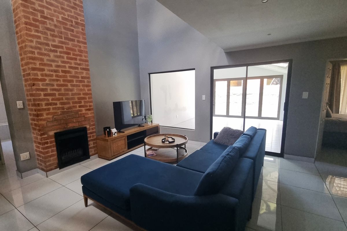 Spacious living room featuring a striking exposed brick fireplace, high vaulted ceilings, large sliding glass doors, and modern tiled flooring.