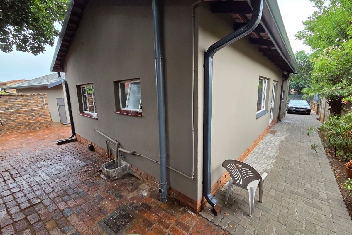 Side view of the house showing paved pathways, exterior wall finishes, downpipes, and window placements.