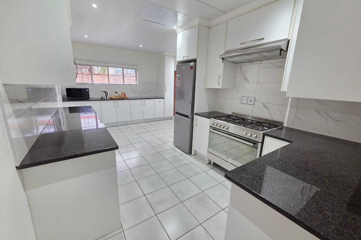Modern kitchen featuring white cabinetry, dark granite countertops, tiled flooring, and a stainless steel gas stove with an integrated extractor fan.