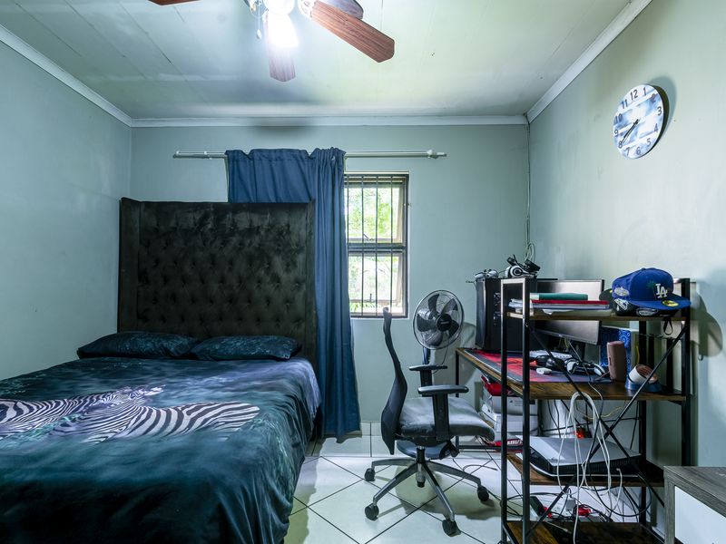 A functional bedroom featuring tiled flooring, a ceiling fan, and security bars on the window, offering a practical space for rest or study.