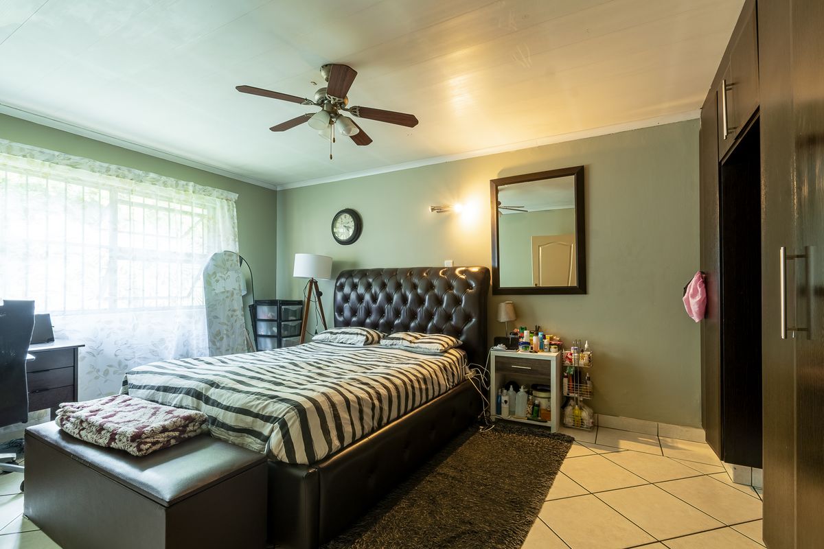 A bedroom featuring tiled flooring, built-in cupboards, and a ceiling fan, with security bars installed on the window.