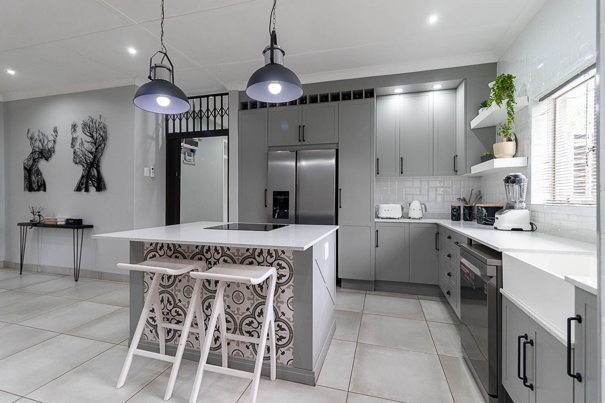 Modern kitchen featuring grey cabinetry, a central island with patterned tile detail, stone countertops, and high-quality finishes throughout.