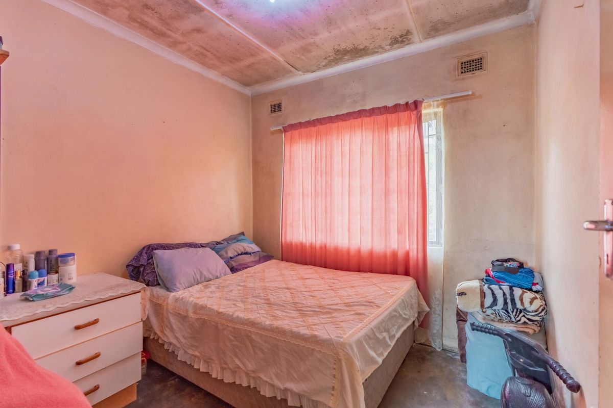 A bedroom featuring a window with curtains and ceiling ventilation. The room requires cosmetic updates to the walls and ceiling finishes.