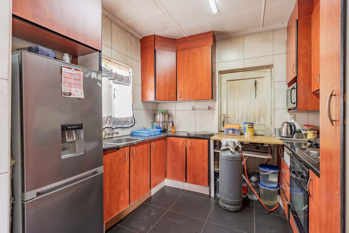 A compact kitchen featuring wood-look laminate cabinetry, tiled backsplash, and built-in cooking appliances, offering a functional layout with potential for modern updates.