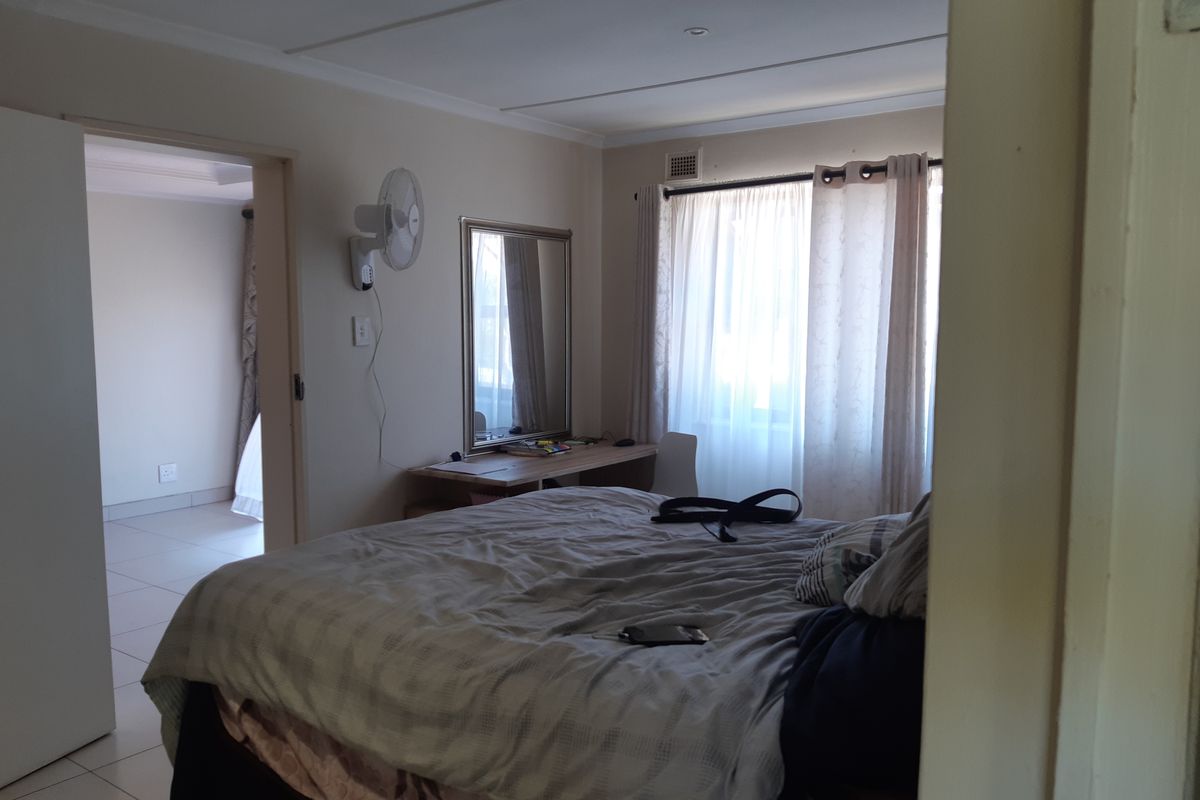 A functional bedroom featuring tiled flooring, a wall-mounted fan, and a built-in desk area with natural light from the window.