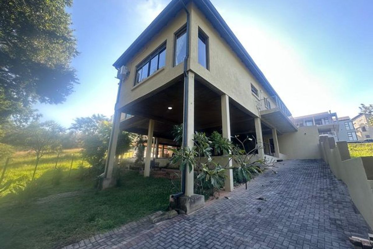 A view of the rear elevation of a multi-level home featuring a stilted design, paved driveway, and an elevated balcony area.
