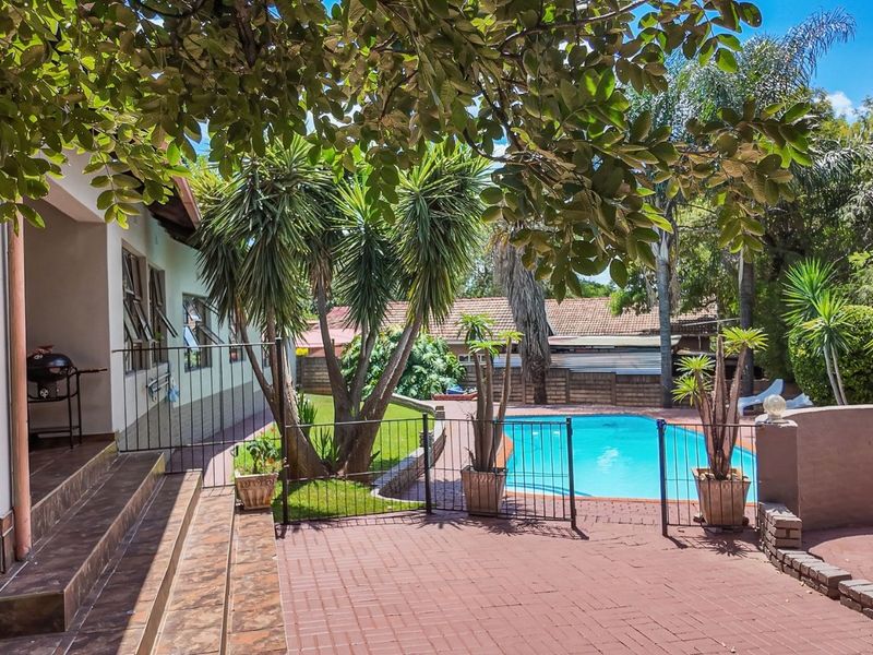 Outdoor entertainment area featuring a swimming pool, paved patio, and secure perimeter fencing, surrounded by established garden landscaping.