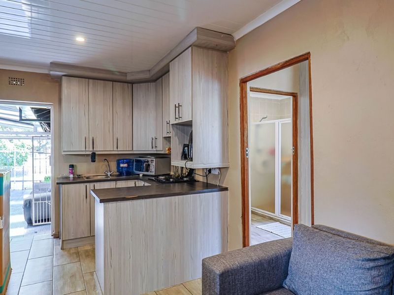 Open plan kitchen area featuring light wood-look cabinetry, dark countertops, and tiled flooring, with direct access to an adjacent bathroom.