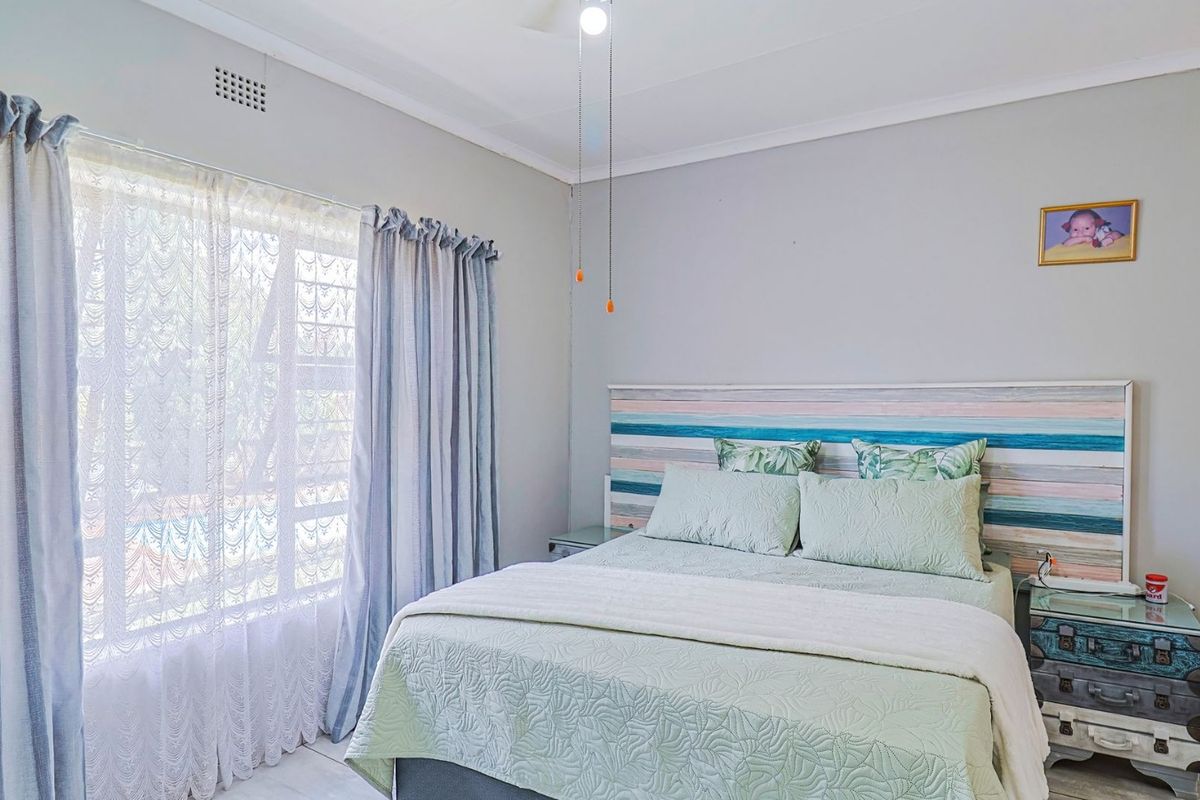 A well-lit bedroom featuring a ceiling fan, security bars on the window, and neutral wall finishes.
