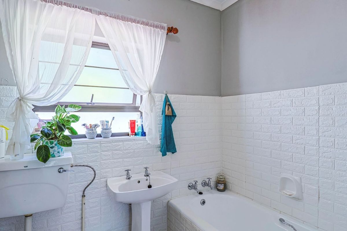 A functional bathroom featuring a pedestal basin, bathtub, and toilet cistern, finished with textured wall tiles and a window for natural light.